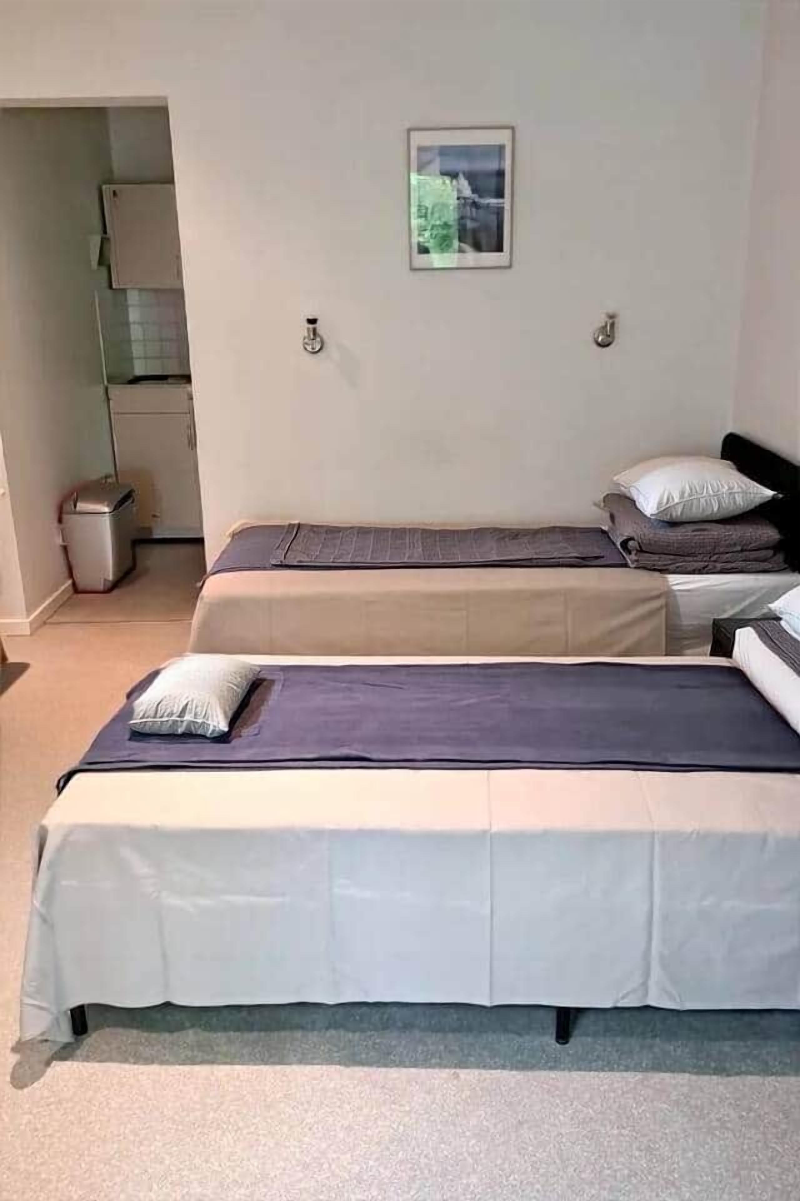 A room with two beds, a small window, and a trash bin.