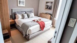 A modern bedroom with a bed, bedside tables, a nightstand, a dresser, and a window with curtains.