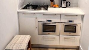 A compact kitchen with a gas stove, two ovens, a countertop, and a small stool.