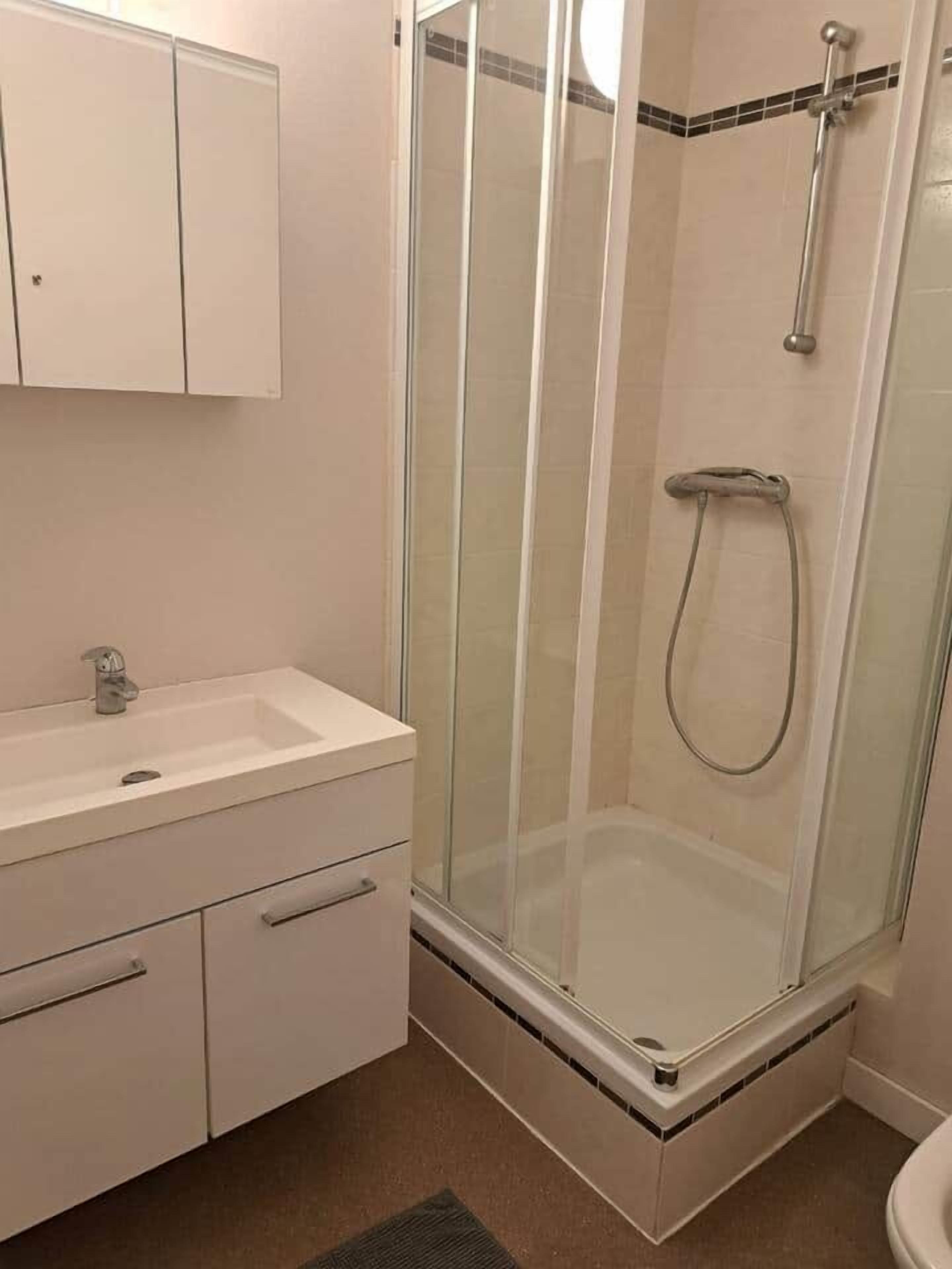 A bathroom with a glass-enclosed shower, a sink, and a cabinet.