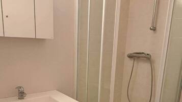 A bathroom with a glass-enclosed shower, a sink, and a cabinet.