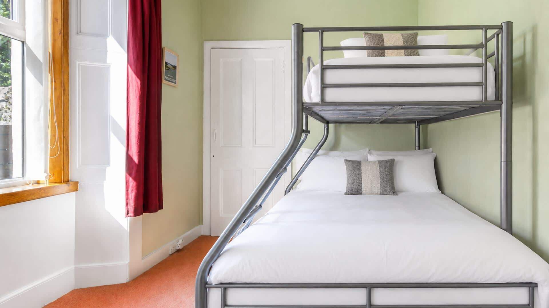 A bunk bed room with a window, a door, and a red curtain.