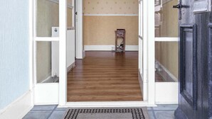 Un couloir avec une porte noire, une porte blanche et une petite table sur laquelle se trouve une lampe.