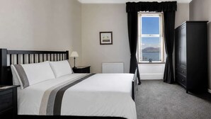Une chambre d’hôtel bien aménagée, avec un lit, une table de chevet, une lampe, un radiateur, une armoire et une fenêtre donnant sur un beau paysage.