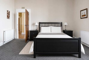 A bedroom with a black four-poster bed, two bedside tables with lamps, a radiator, and a door leading to another room. - Scenic Waterfront Apartment with Stunning Loch Views (Port Bannatyne)