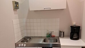 Una cucina compatta con fornello, lavello e macchina da caffè sul piano di lavoro.