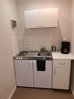 A compact kitchen with a stove, sink, and a coffee maker on the counter.