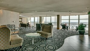 Ein geräumiger Loungebereich mit einem gemusterten Boden, bequemen Sitzmöglichkeiten und großen Fenstern mit Meerblick.