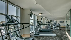 Ein Fitnessstudio mit Laufbändern, Crosstrainern und Kraftgeräten, großen Fenstern und Blick auf die Stadt.