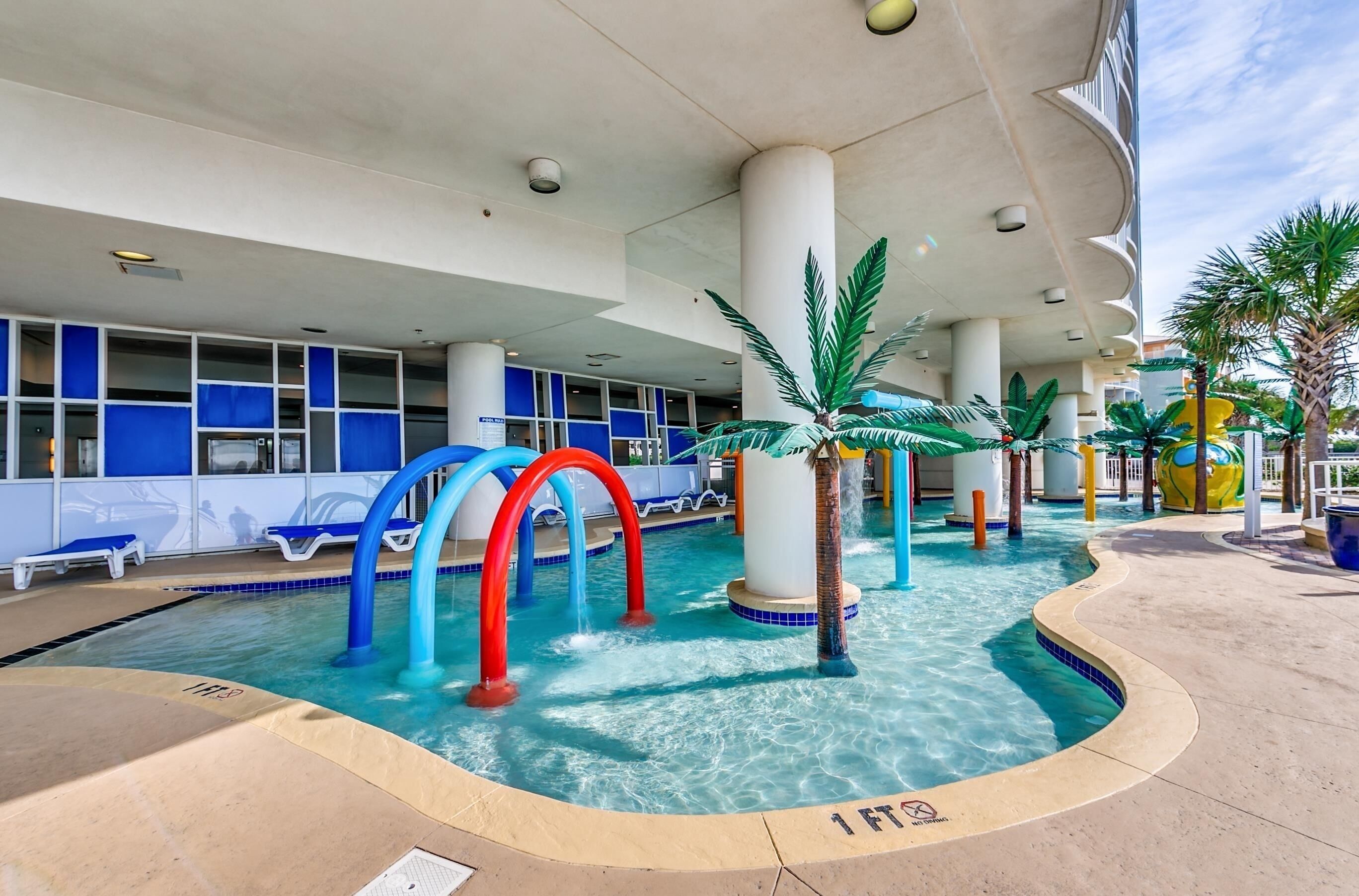 A pool area with clear water, blue and red arch structures, and palm trees.