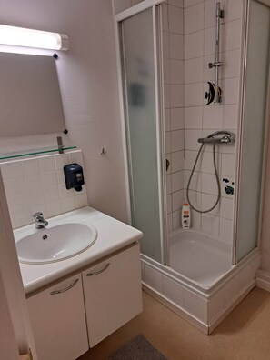 Un bagno con lavandino, specchio, box doccia in vetro e doccetta.
