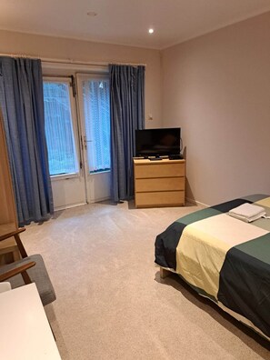 A hotel room with a bed, a TV on a wooden dresser, a chair, and a window with curtains.
