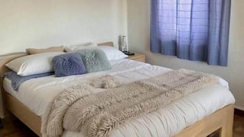 Een slaapkamer met een houten bed, een nachtkastje, een wandlamp en een raam met gordijnen.