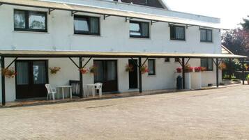 Een gebouw met twee verdiepingen, een overdekte patio, buitenzitplaatsen en bloembakken.
