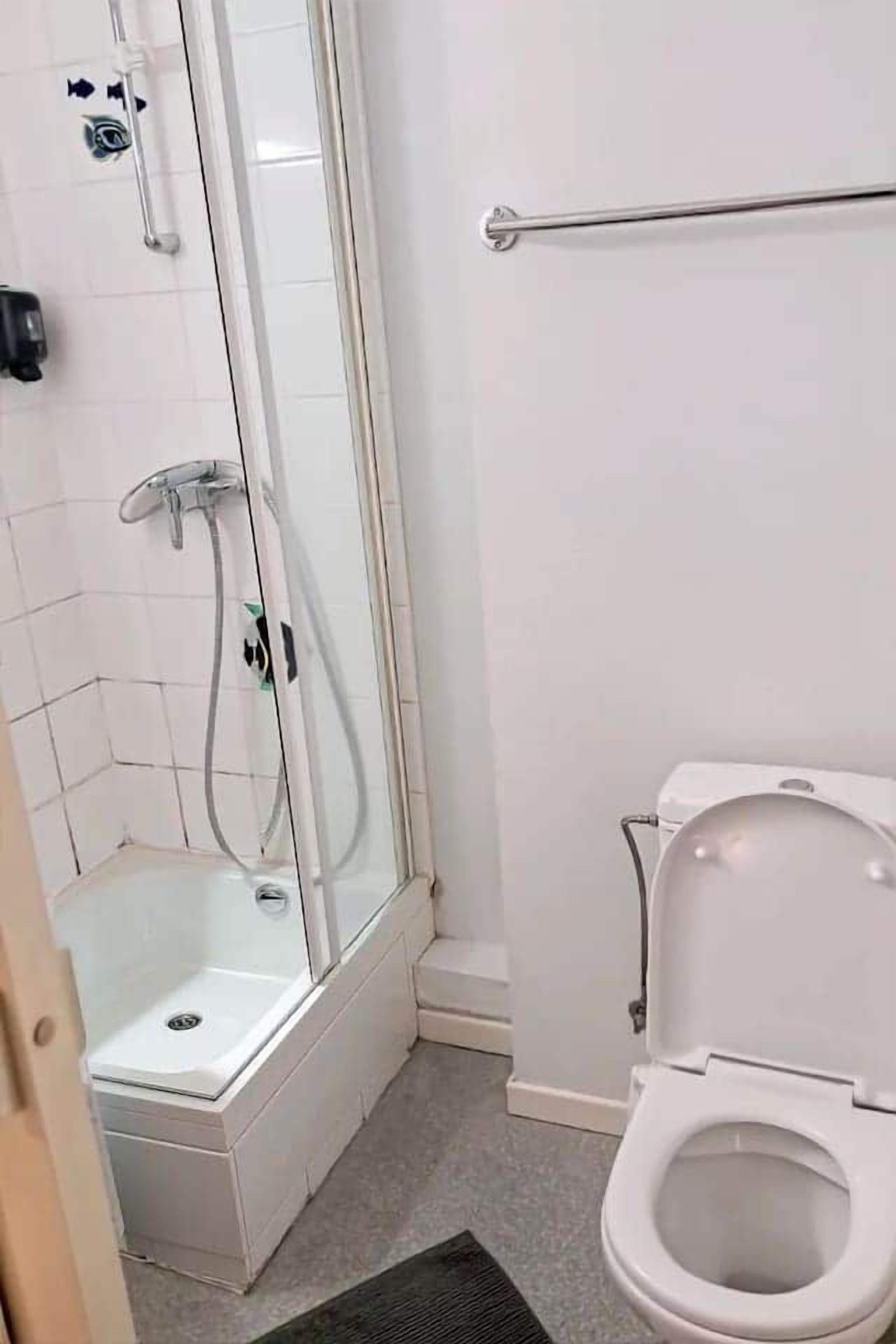 Een badkamer met douche, toilet en een handgreep.