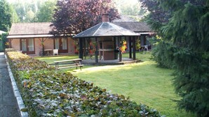 Un bâtiment à la façade en briques, un pavillon couvert, une pelouse et une haie.