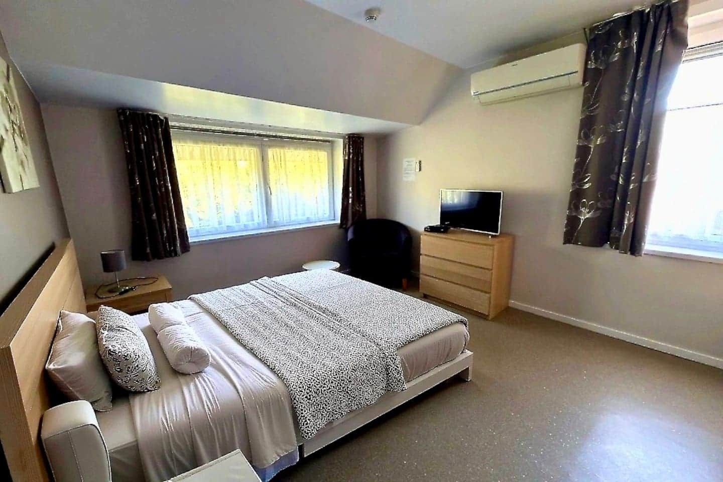 Un dormitorio con una cama, un televisor en una cómoda, una silla y una ventana con cortinas.