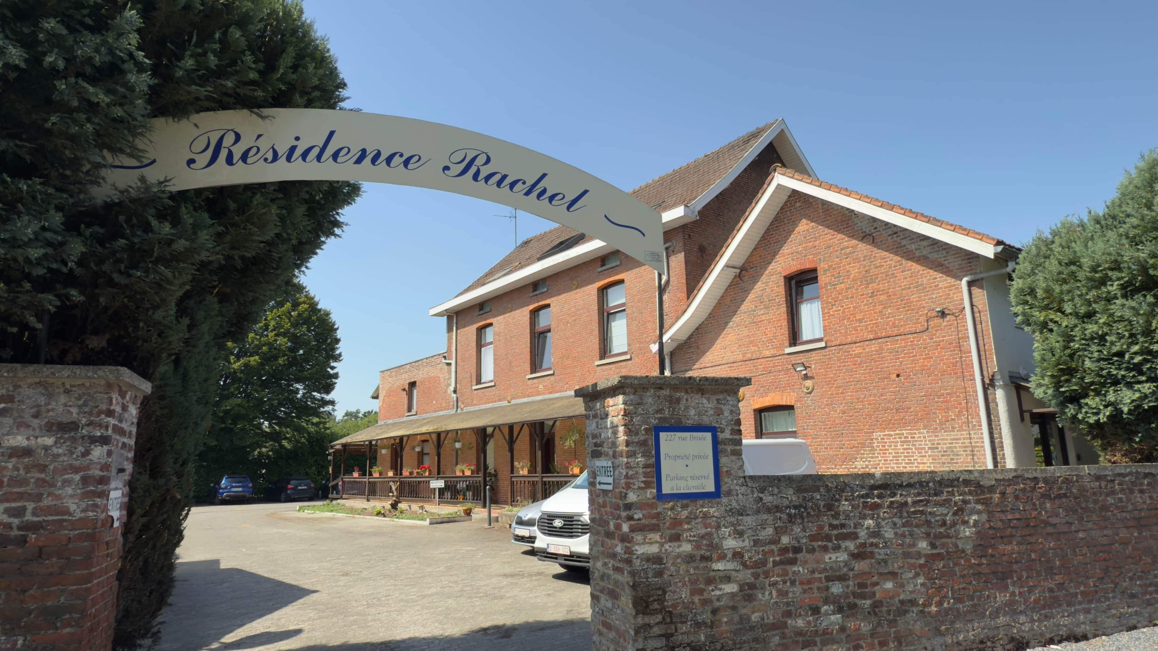Un edificio in mattoni con un cartello che riporta 'Résidence Rachel' e un'area d'ingresso coperta.