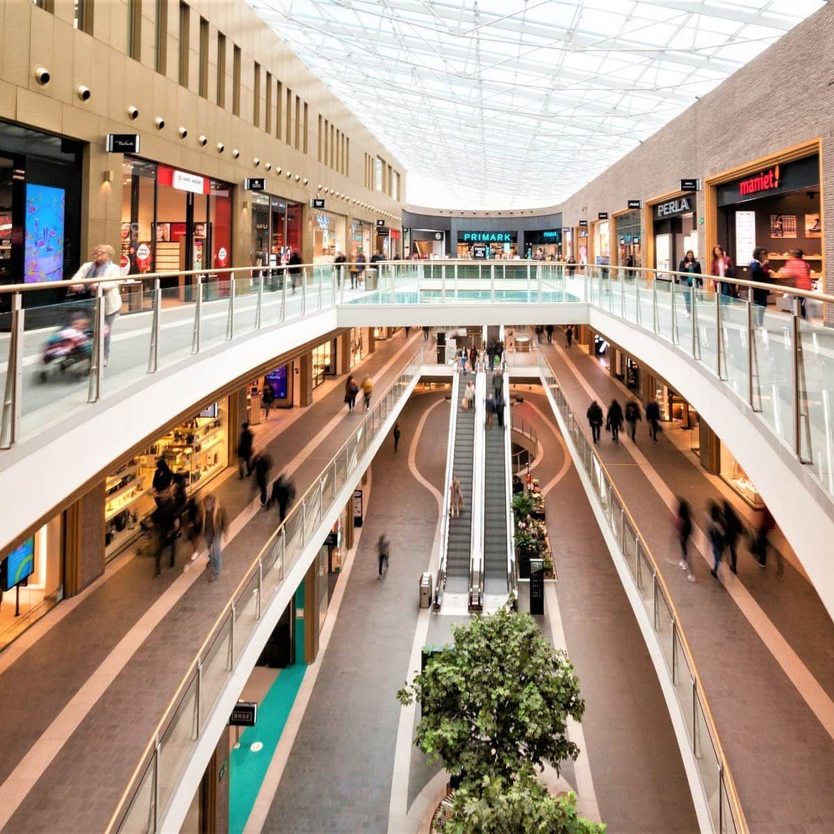 Un centre commercial à plusieurs niveaux, doté d'un escalier mécanique central, de rampes en verre et de divers magasins de vente au détail.