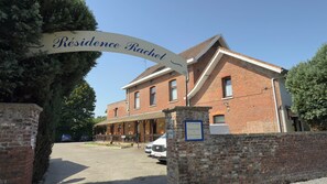 Un bâtiment en briques avec une enseigne indiquant « Résidence Rachel » et un espace d’entrée abrité.