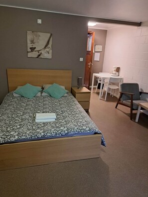 Une chambre à coucher comprenant un lit, une table de chevet, une chaise, une petite table avec une machine à café, et une porte donnant sur une autre pièce.