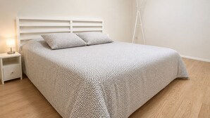 A bedroom with a bed, white headboard, bedside table, lamp, and a white floor lamp.