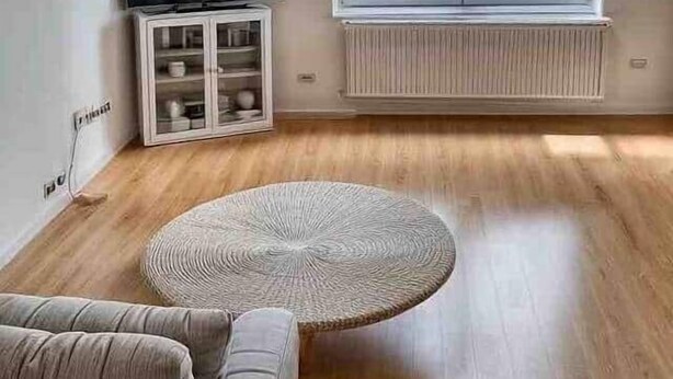 A living room with a sofa, a round coffee table, a TV on a cabinet, and a large window with a view of buildings.