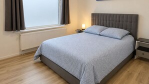 A bedroom with a bed, a window with curtains, a nightstand, a lamp, and a painting on the wall. - Jumet 242 D'Bruxelles-charleroi-airport (Charleroi)