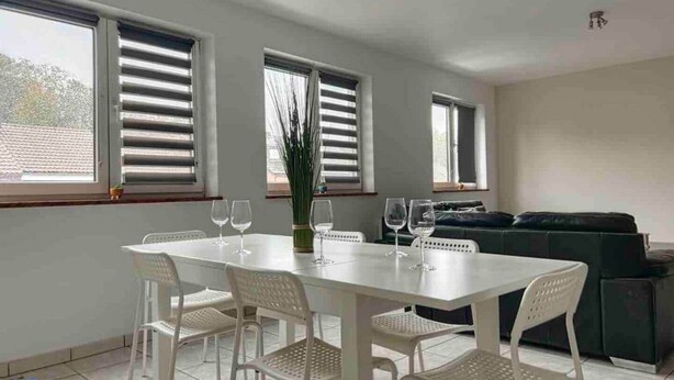 Un comedor con una mesa y sillas blancas, una planta verde y un sofá al fondo.