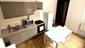 A compact kitchen with a sink, stove, microwave, and a small refrigerator. There is a white dining table with chairs.
