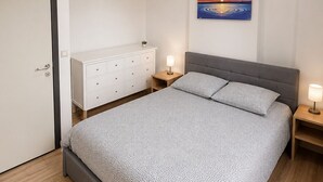A bedroom with a bed, bedside tables, a nightstand, a painting, and a ceiling light.