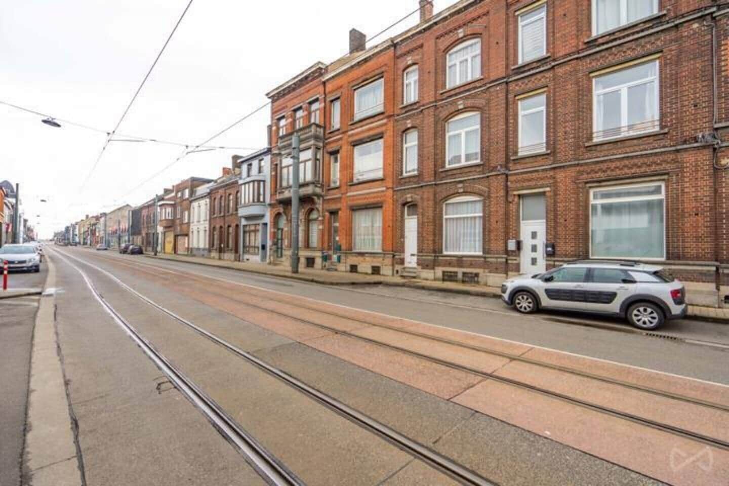 Eine Straße mit Straßenbahnschienen, Backsteingebäuden und parkenden Autos.