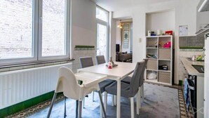 A modern kitchen with white cabinetry, a dining table with chairs, and a view of a brick wall through large windows.