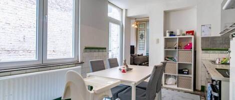 Una cocina moderna con armarios blancos, una mesa de comedor con sillas y vistas a un muro de ladrillo a través de amplios ventanales.