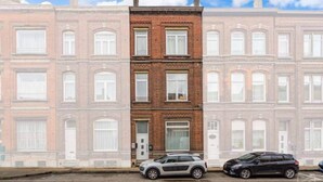 A row of terraced houses with a central brick building, two cars parked in front, and a clear sky.