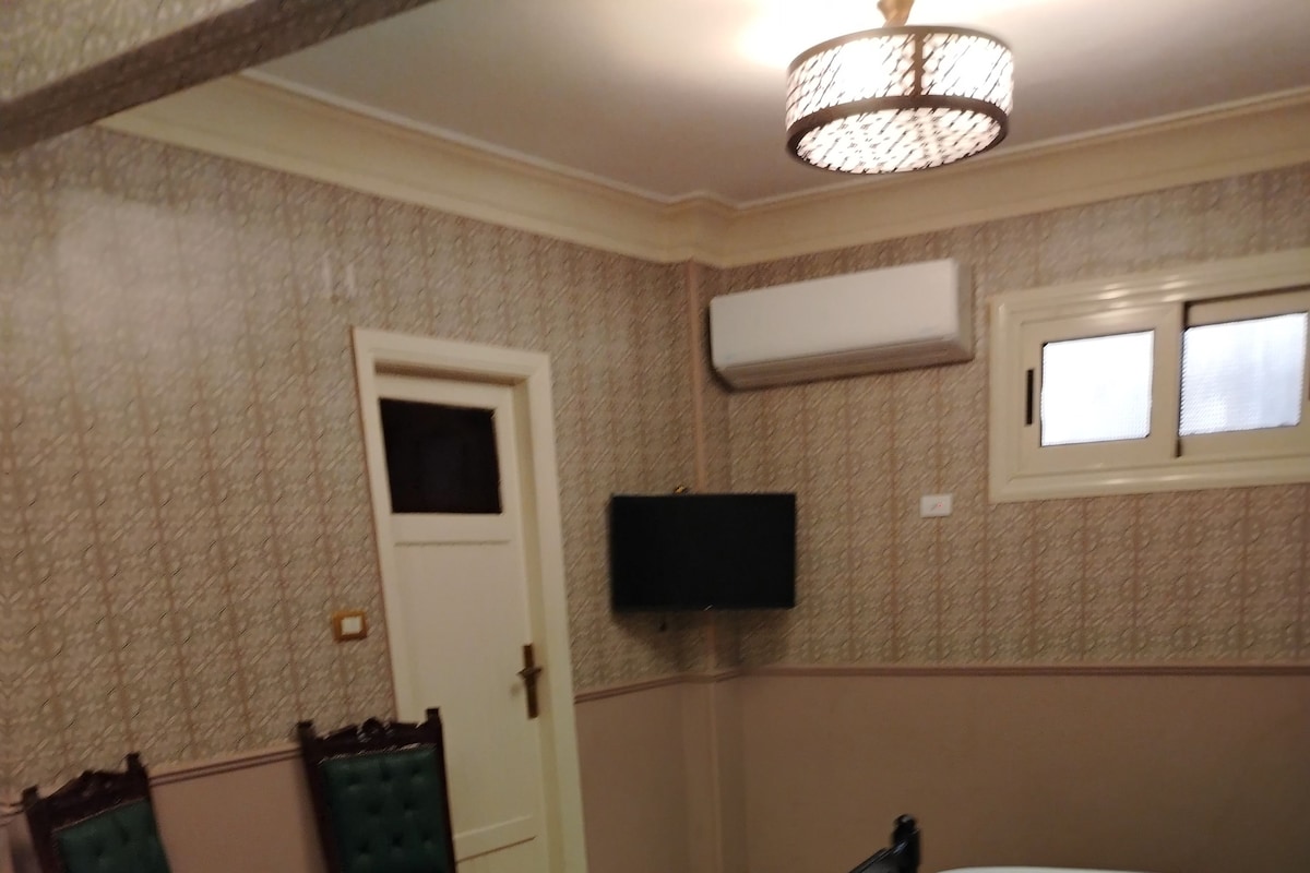 Quarto de hotel com duas camas, uma televisão fixada na parede, uma mesa pequena e duas cadeiras.