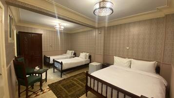 Habitación de hotel con dos camas individuales, una cama grande, un escritorio, una silla, un armario y papel tapiz estampado.