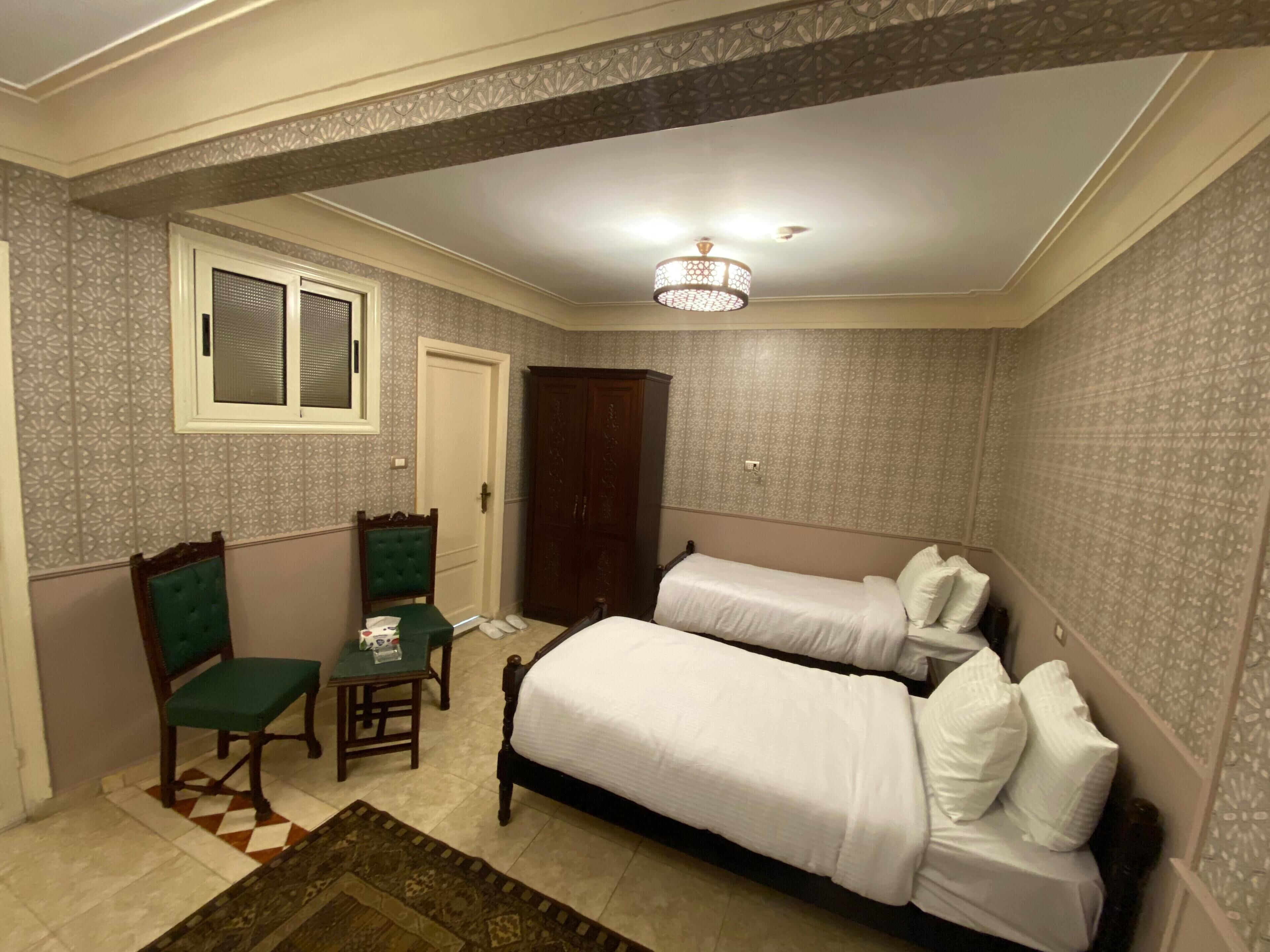 A bedroom with two beds, a chair, a small table, and a door.