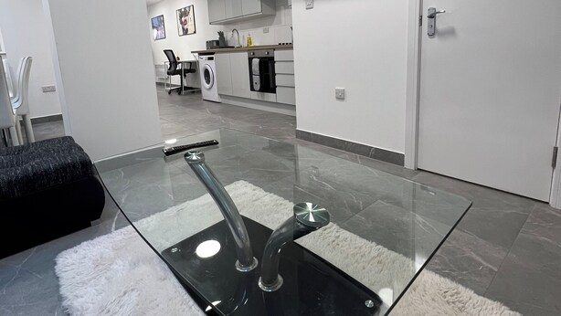 A modern kitchen with a glass dining table, a flat-screen TV, and a washing machine. - Stylish 3BR Appartment - West Hampstead - Sleeps up to 8 - NearTube - (London)