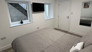 A bedroom with a large bed, a small window, a television, and a door. - Stylish 3BR Appartment - West Hampstead - Sleeps up to 8 - NearTube - (London)