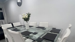 A modern dining area with a glass-top table, white chairs, and a vase with flowers. - Stylish 3BR Appartment - West Hampstead - Sleeps up to 8 - NearTube - (London)