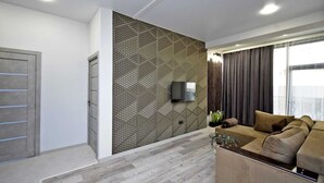 A modern living room with a geometric patterned wall, a flat-screen TV mounted above it, a sofa with cushions, and a glass coffee table. - 2-bedroom apartment in fantastic Yerevan with WiFi, AC (Yerevan)