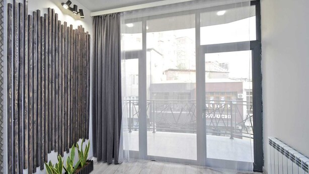 A modern room with a large sliding glass door leading to an outdoor balcony, a wooden wall panel, and a potted plant. - 2-bedroom apartment in fantastic Yerevan with WiFi, AC (Yerevan)