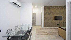 A modern kitchen with a built-in oven, a dining area with a glass table and wireframe chairs, and a patterned wall with a mounted TV. - 2-bedroom apartment in fantastic Yerevan with WiFi, AC (Yerevan)