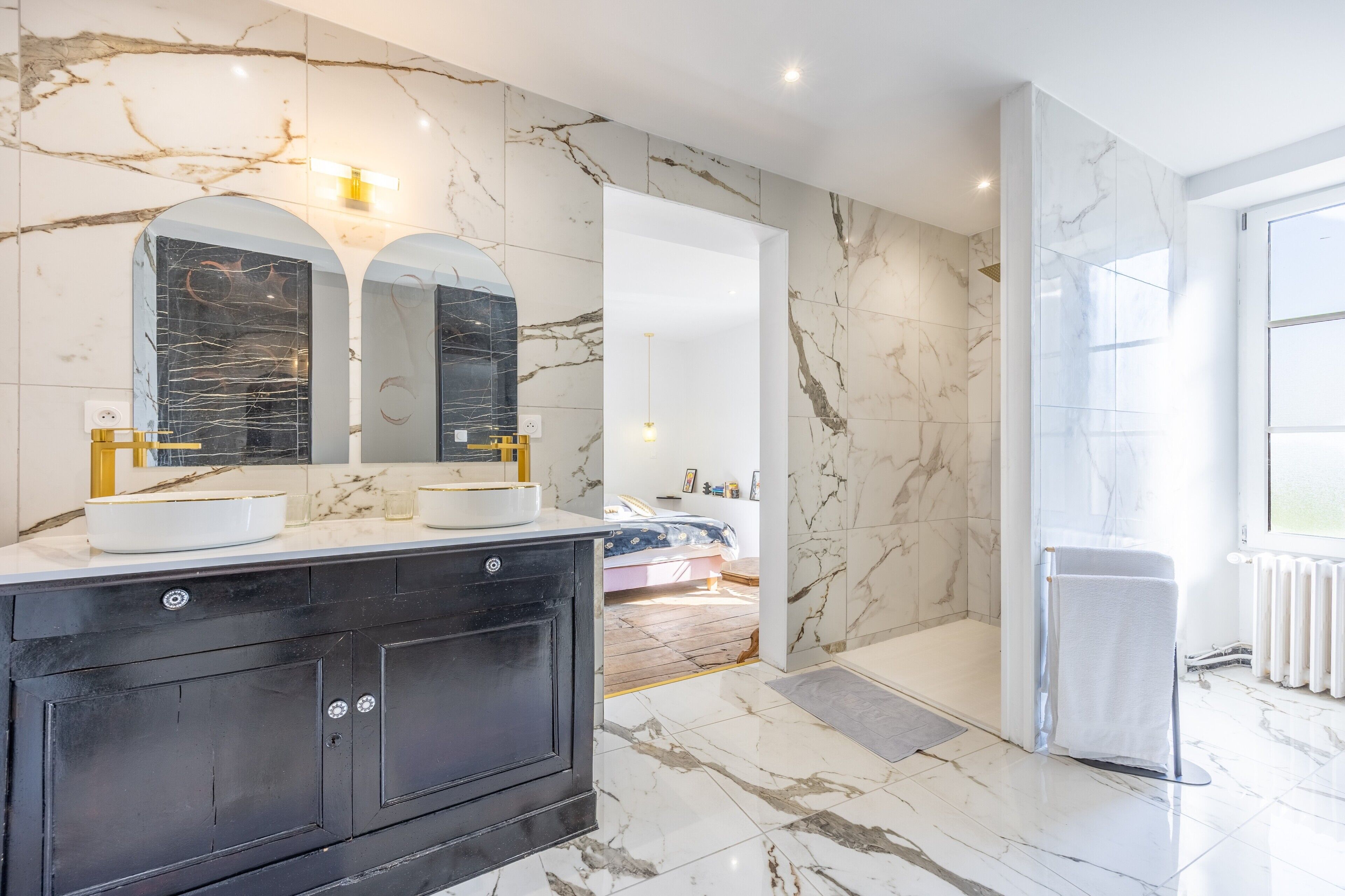 A modern bathroom with marble walls, a black vanity, dual sinks, and a large mirror.