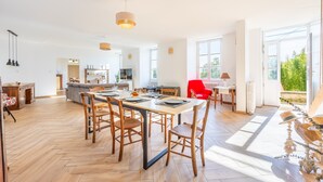 Un espacio habitable amplio con una mesa de comedor, sillas y una butaca roja. Se observa una zona de cocina al fondo con un refrigerador y un microondas.