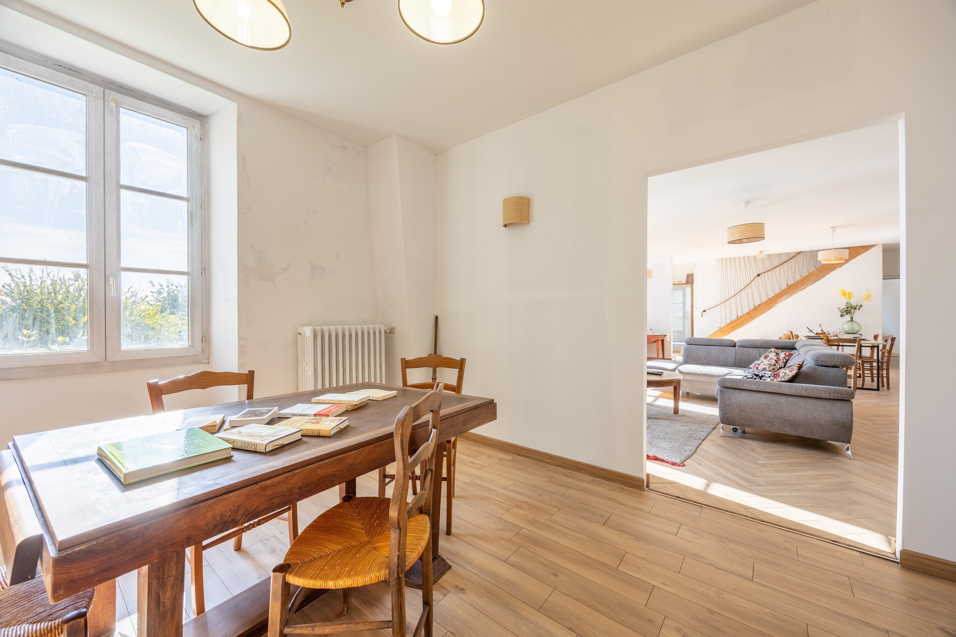 Ein Essbereich mit Holztisch und -stühlen, einem Heizkörper und Blick auf ein Wohnzimmer mit Sofa und Treppe.