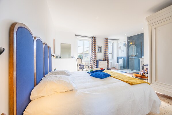 A hotel room with a large bed, a bathroom with a glass shower, and a view of the outside.
