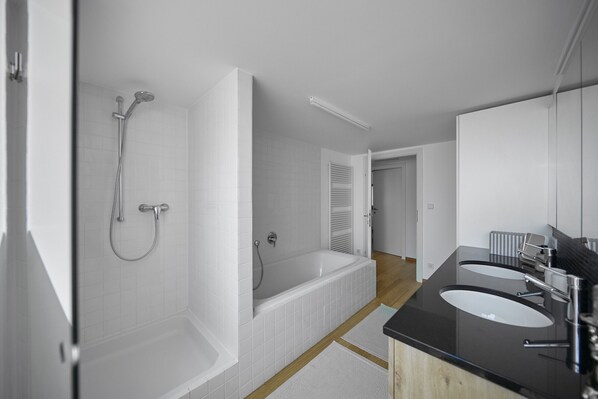 A modern bathroom with a bathtub, two sinks, and a large mirror.