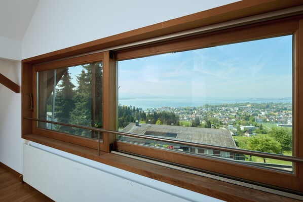 A room with a large window overlooking a cityscape and a body of water. - 9602 Berg-Loft Bregenz (Lochau)